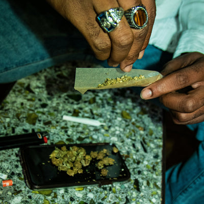Person rolling a joint with cannabis buds on a concrete surface.